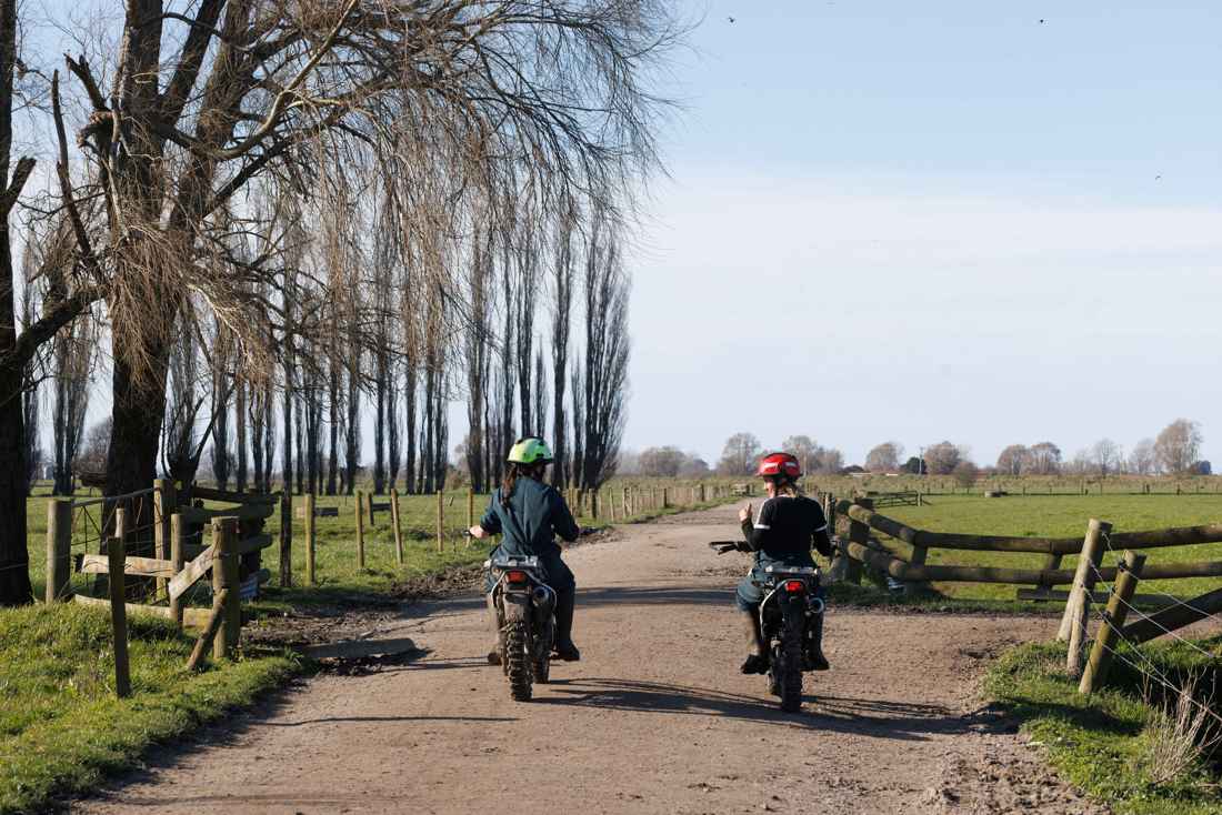 Two individuals riding motorcycles on a dirt road with their helmets on