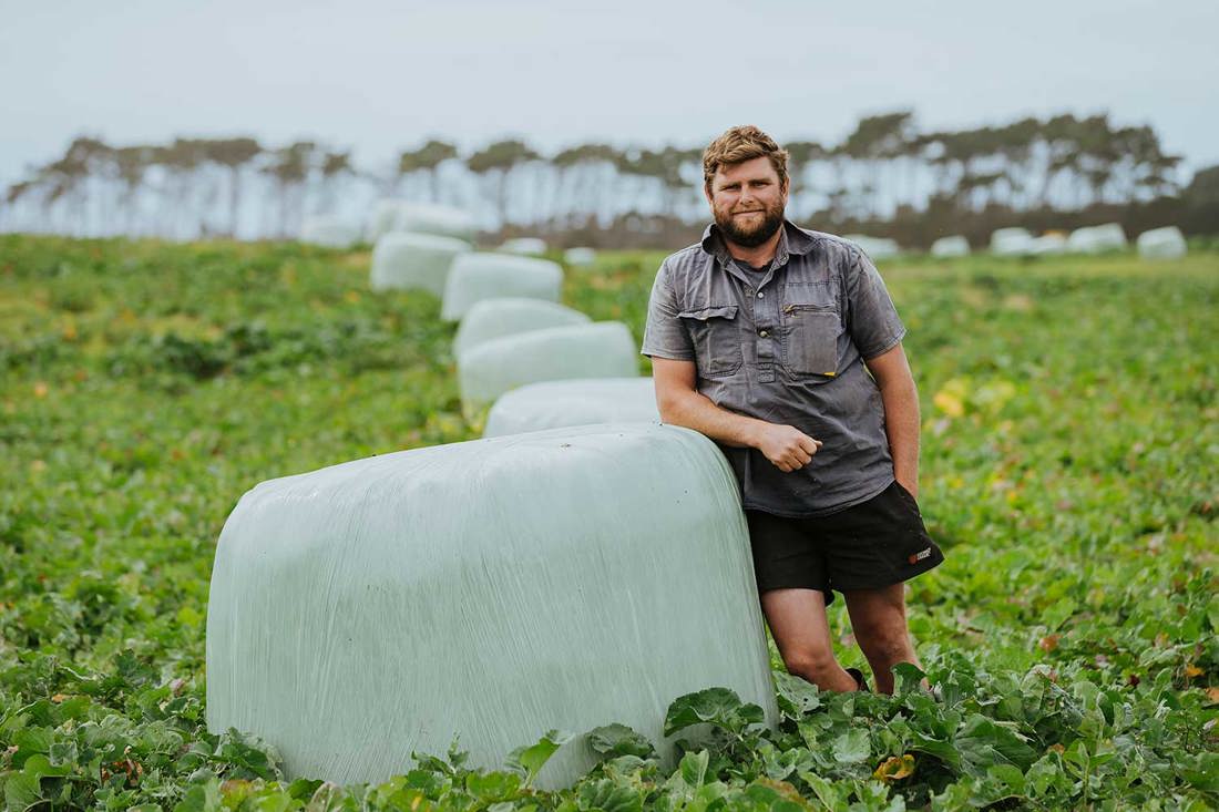 Dairy farmer Luke Templeton in a crop paddock leaning on a wrapped silage bale