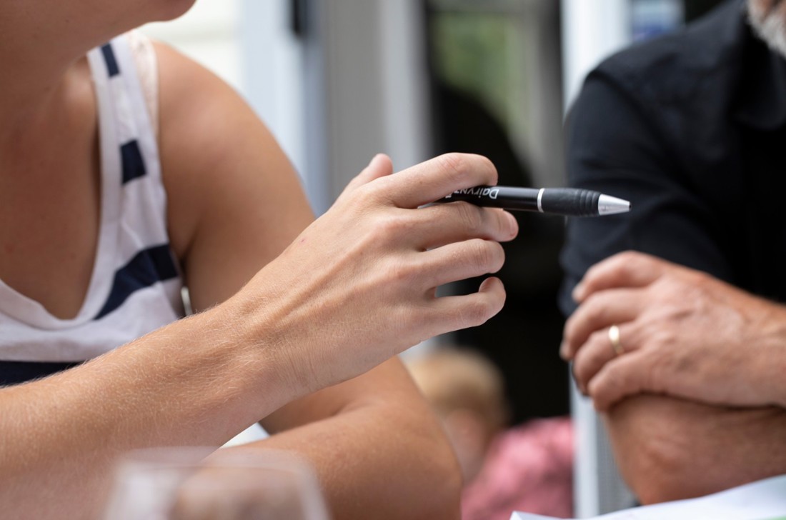 Two people sitting at an outdoor table talking about work, one is holding a pen.