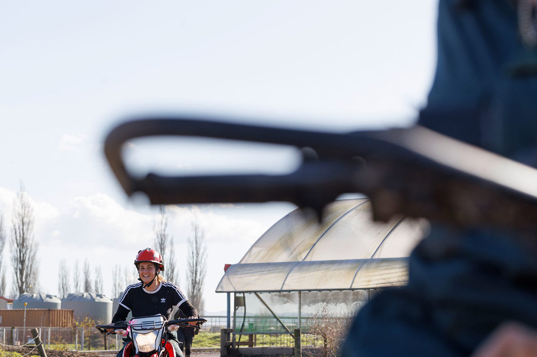 Farm workers riding farm motorbikes along a farm track wearing helmets.