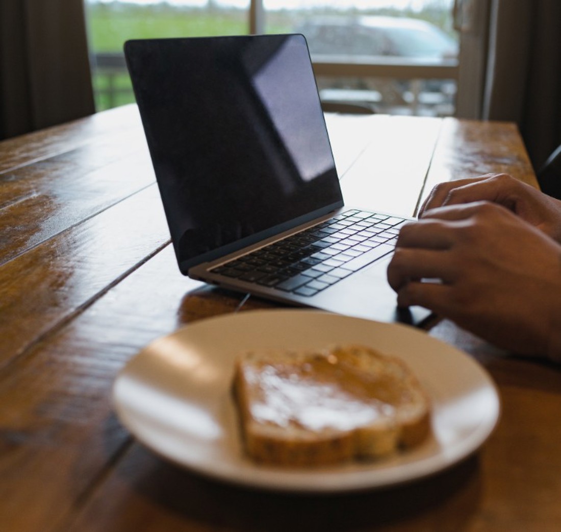 A close up of a laptop on a kitchen table with toast on a plate next to it