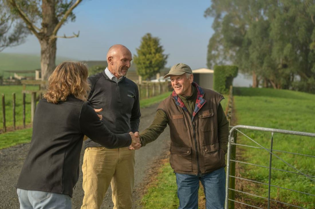 Two DairyNZ regional team members at a farm entrance meeting a dairy farmer.