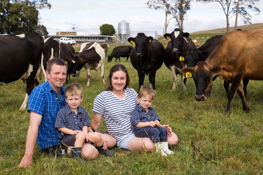 The Whitaker family sitting on the grass in a paddock on their dairy farm with cows in the background
