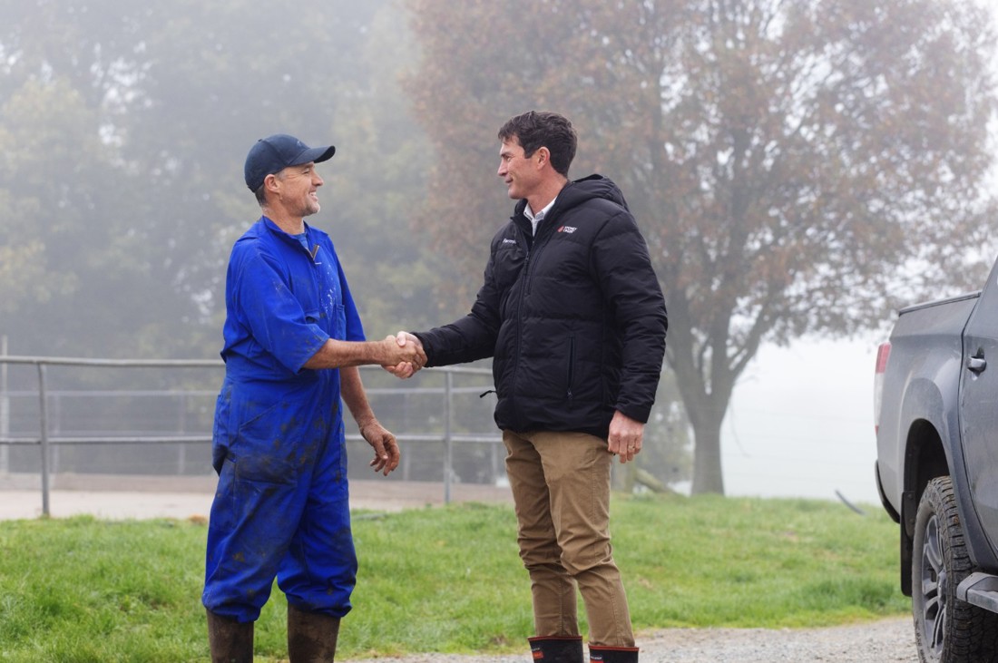 A farm consultant shaking hands with a dairy farmer outside on a misty morning