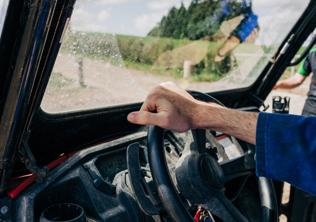 A hand holding a farm vehicle's steering wheel